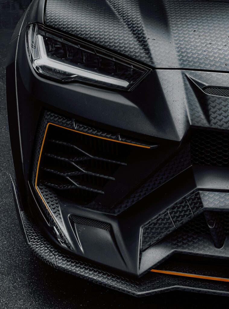 Detailed shot of a luxury sports car's front with carbon texture and sleek design.